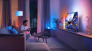 Ein Mann spielt ein Game desssen Farben und Lichter von dem PHILIPS Hue Play Gradient Lightstrip nachgeahmt werden und im Raum zu sehen sind