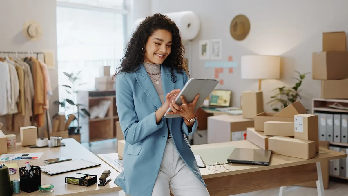 Eine Frau lehnt an einem Tisch und tippt auf ihrem Tablet.