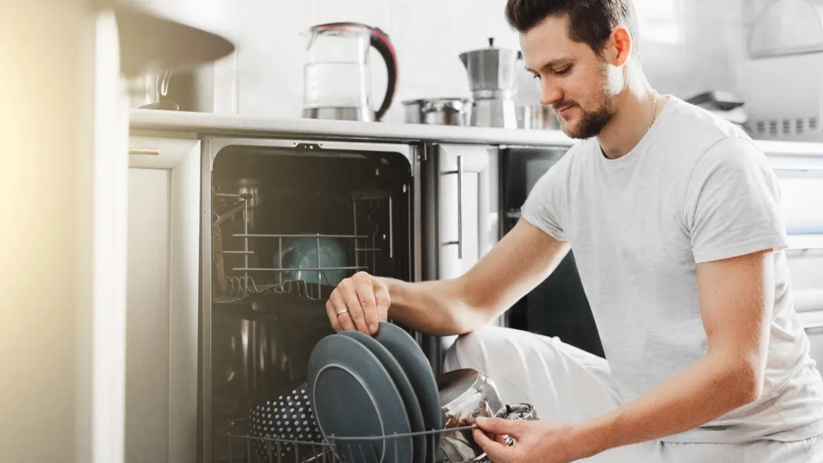 Ein Mann räumt Geschirr aus einem Geschirrspüler aus.