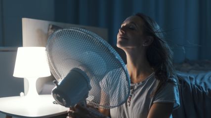 Eine Frau hält sich einen großen Ventilator vor das Gesicht.