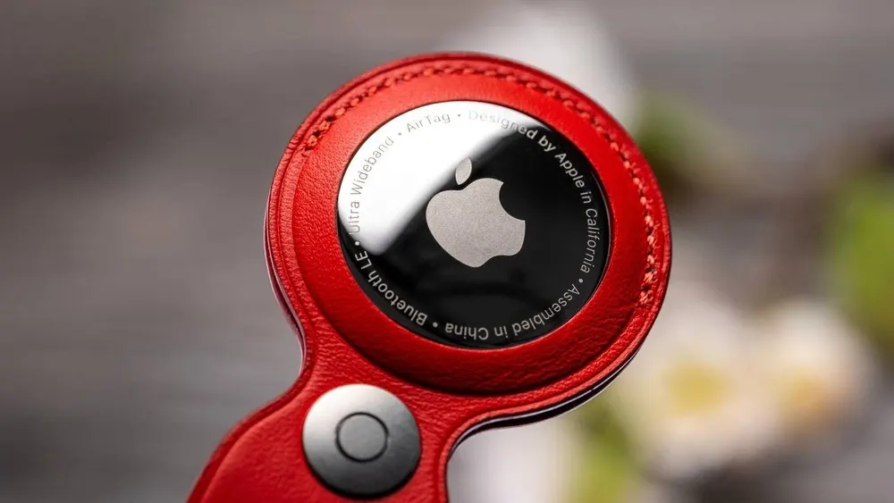 Nahaufnahme eines Apple AirTag in roter Lederhülle mit Apple-Logo auf silberner Metallplatte.