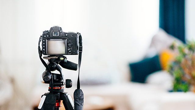 Eine schwarze Kamera auf einem Stativ steht vor einem unscharfen Hintergrund mit Kissen und einer Pflanze.