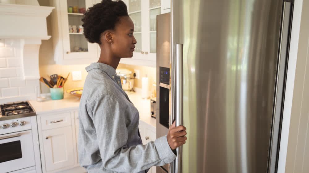 Eine Frau steht vor einem geöffneten Kühlschrank.