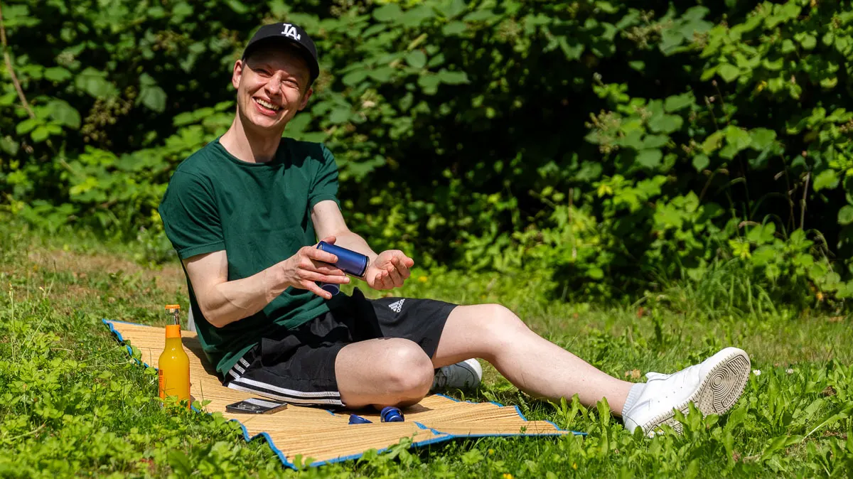 Alex sitzt auf einer Strandmatte im Park und kühlt sein Handgelenk mit der InstaChill-Kühlplatte des Shark ChillPill.