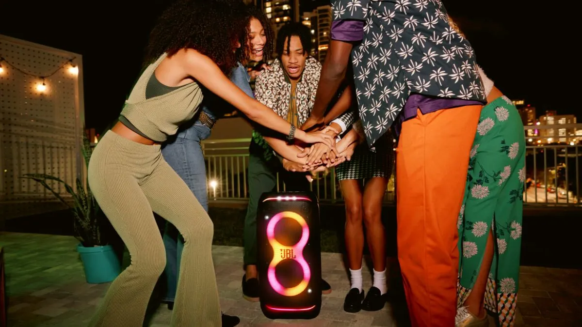 Fünf junge Menschen stehen auf einer Terrasse und halten ihre Hände über die JBL PartyBox Stage 320.
