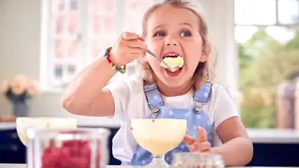 Ein Mädchen nimmt einen großen Löffel mit Vanilleeis in den Mund.