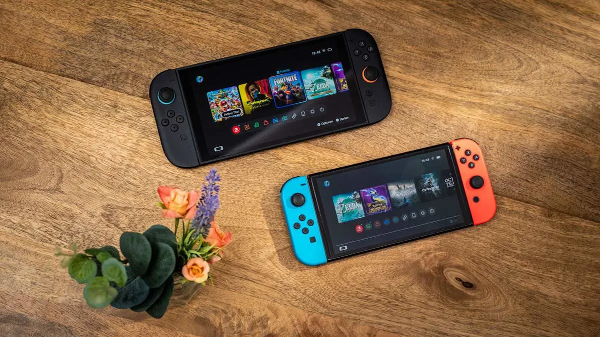 Eine Nintendo Switch 2 und eine Nintendo Switch liegen schräg versetzt auf einem Holztisch.