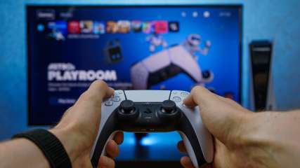 Eine Person sitzt vor einem Bildschirm und hält einen PlayStation Controller in den Händen.