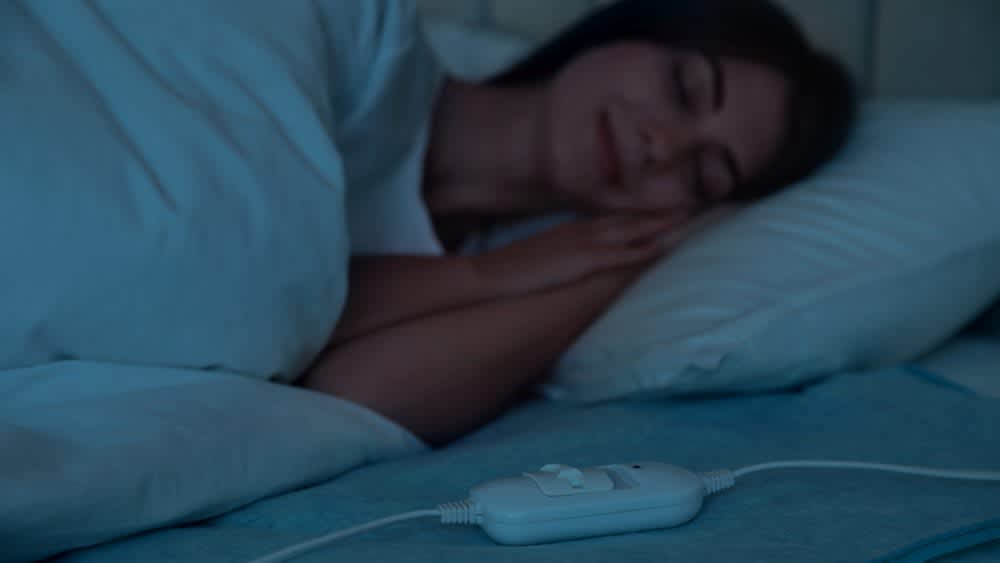Frau schläft mit Heizdecke Fernbedienung im Vordergrund