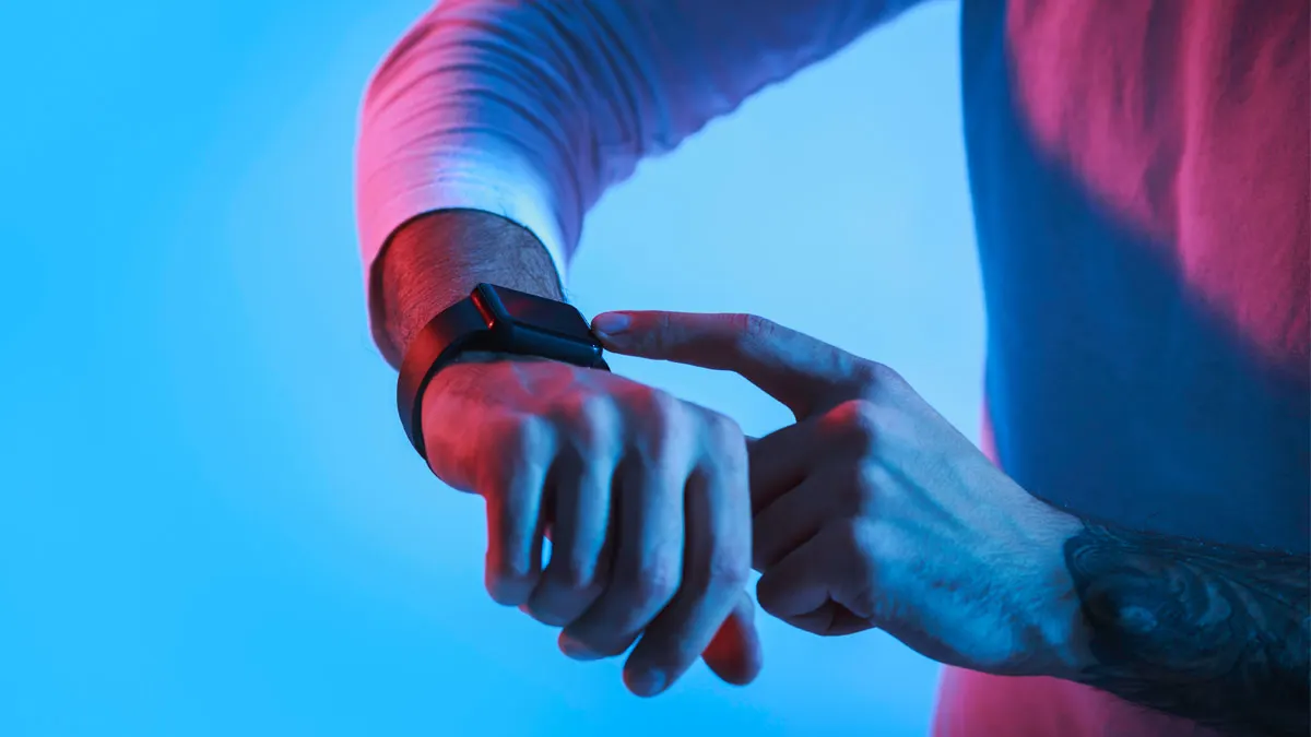 Eine Hand mit einer Smartwatch wird von der anderen Hand bedient. Der Hintergrund ist blau.