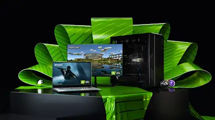 Ein Laptop, ein Monitor, ein PC-Turm und grüne Dekoration auf einem schwarzen Tisch vor schwarzem Hintergrund.