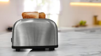 Zwei fertig geröstete Toastscheiben stecken in einem Doppelschlitz-Toaster, der auf einer Arbeitsplatte steht.