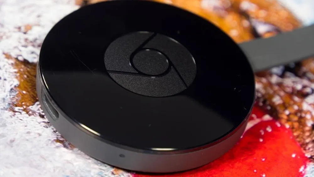Ein schwarzer, runder Google Chromecast liegt auf einem farbigen Untergrund mit abstraktem Muster und einem grauen Kabel.
