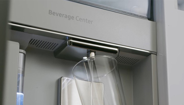 Ein Glas wird an einer grauen Getränkeausgabe mit silbernem Hebel befüllt. Der Schriftzug "Beverage Center" ist sichtbar.