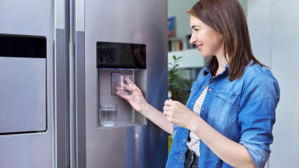 Eine Frau holt sich am Wasserspender eines Side-by-Side-Kühlschranks ein Glas Wasser.