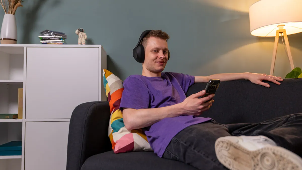 Alex sitzt auf einem Sofa und steuert den Kopfhörer Sony WH-1000XM6 mit seinem Smartphone.