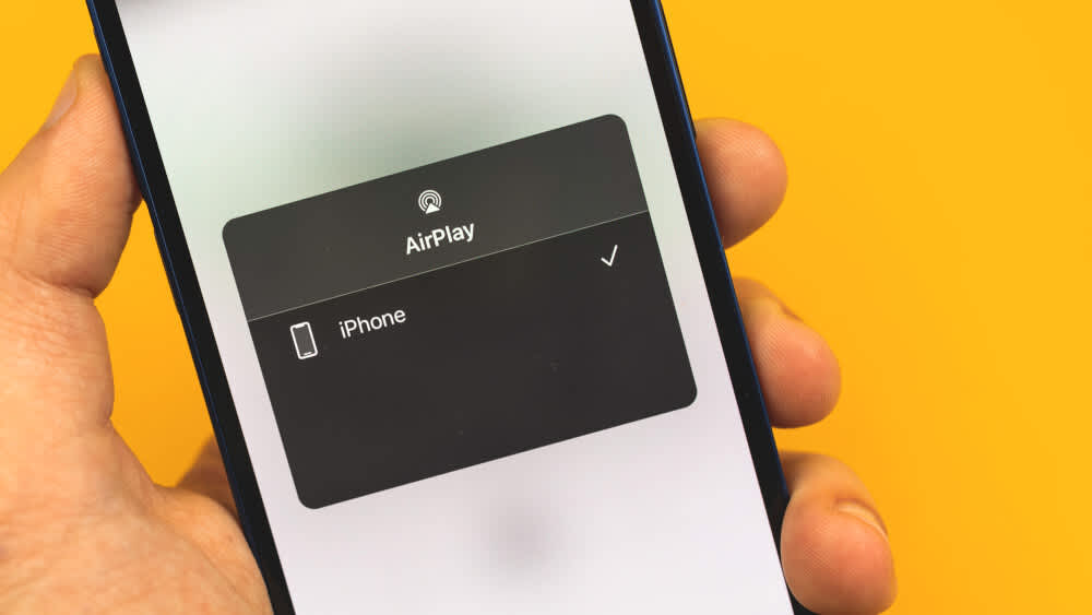 Eine Person hält ein iPhone in der Hand auf dem die Funktion "AirPlay" eingeschaltet ist.