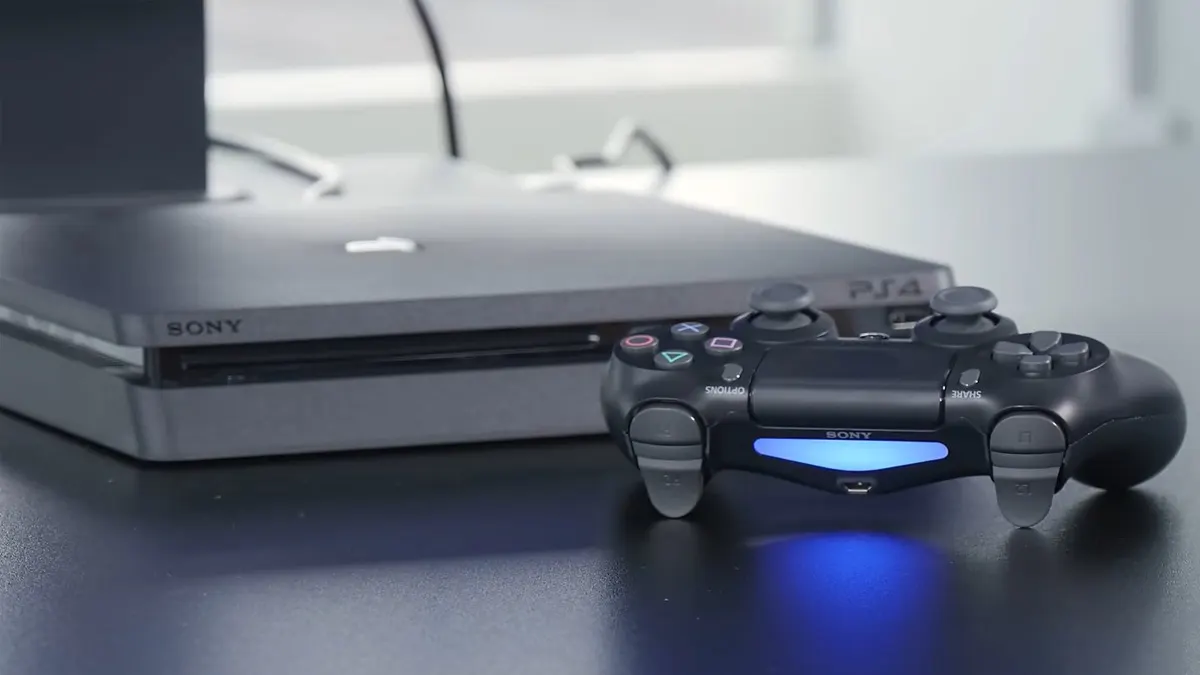 Schwarze Playstation 4 auf einem schwarzen Tisch. Davor liegt ein schwarzer Controller, der blau leuchtet.