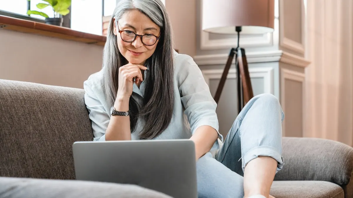 Eine ältere Frau sitzt mit einem Laptop auf dem Sofa.