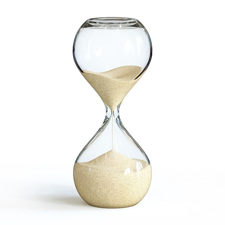 Eine Sanduhr aus Glas, teilweise gefüllt mit beigem Sand, steht vor einem weißen Hintergrund.