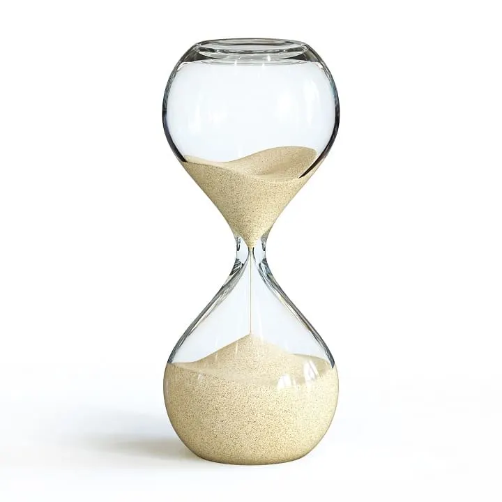 Eine Sanduhr aus Glas, teilweise gefüllt mit beigem Sand, steht vor einem weißen Hintergrund.