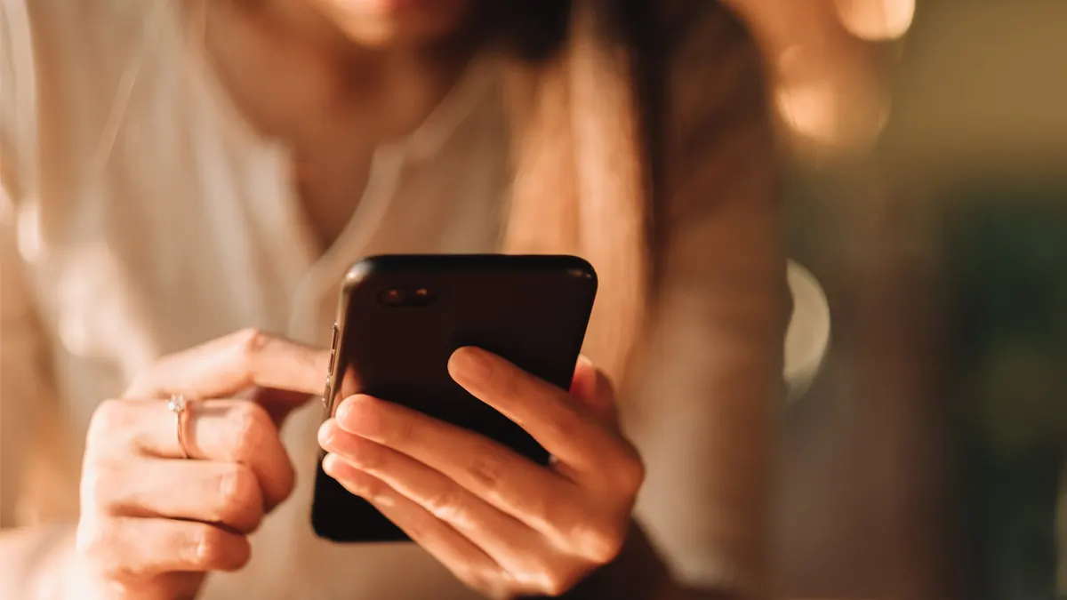 Frau tippt mit ihren Fingern auf einem schwarzen Smartphone. 