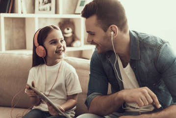 Ein Mädchen und ein Mann mit Kopfhörern schauen auf ein Tablet