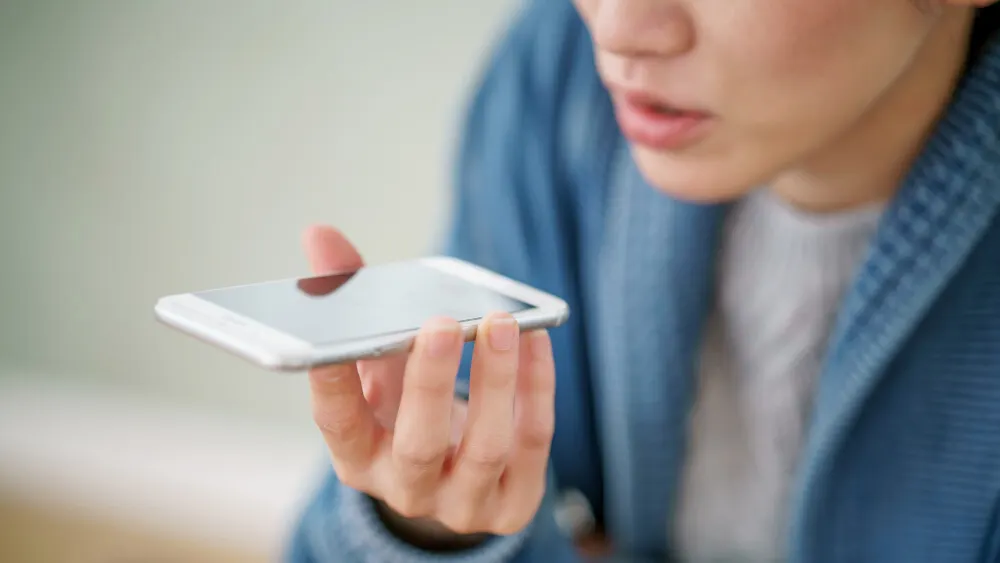 Eine Person in einem blauen Bademantel hält ein silbernes Smartphone waagerecht in der Hand und spricht.