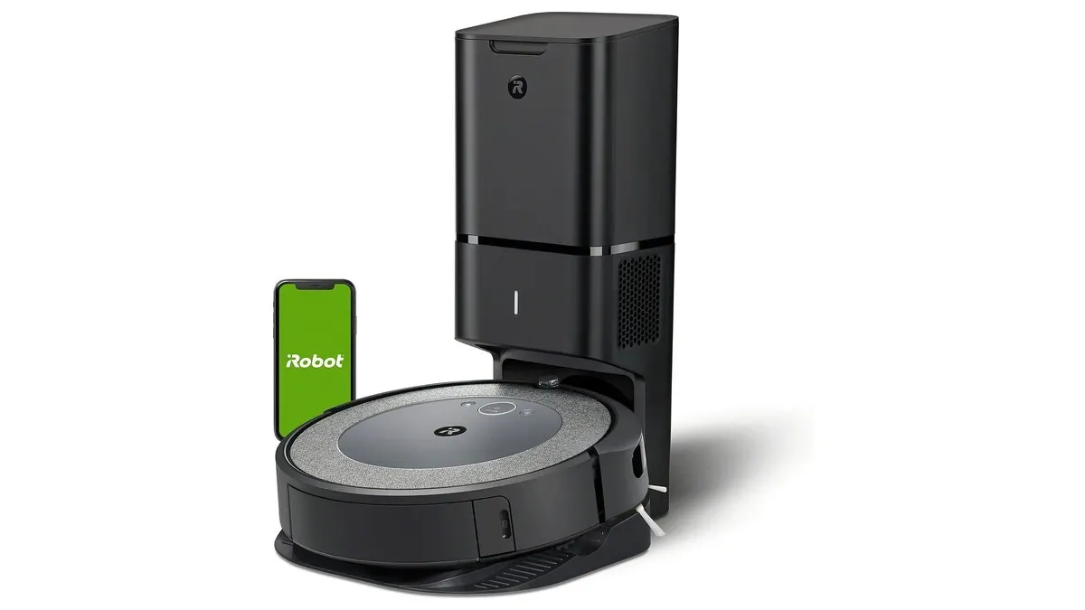 Der Saugroboter iRobot Roomba i5+ an seiner Absaugstation, dahinter ein Smartphone, das die iRobot-App zeigt.