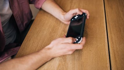 Arme einer Person, die eine Spelkonsole in der Hand hält