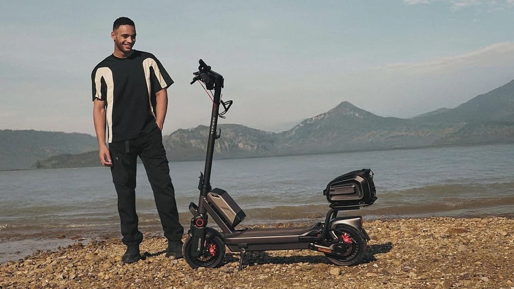 SEGWAY Ninebot MAX G3 D E-Scooter am Seeufer, Mann steht daneben und lächelt, vor weiter Bergkulisse.