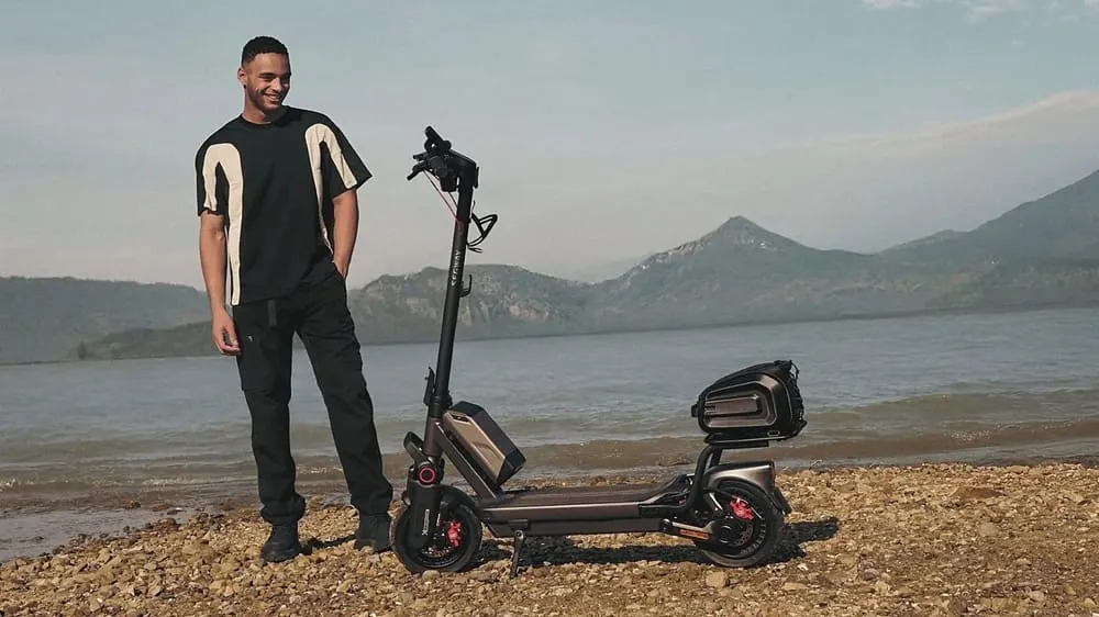 SEGWAY Ninebot MAX G3 D E-Scooter am Seeufer, Mann steht daneben und lächelt, vor weiter Bergkulisse.