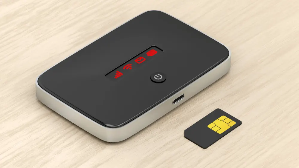 Ein schwarzer, rechteckiger WLAN-Router mit silberfarbenen Kanten und einer SIM-Karte auf einem hellbraunen Holztisch. Rote Symbole leuchten auf dem Router.