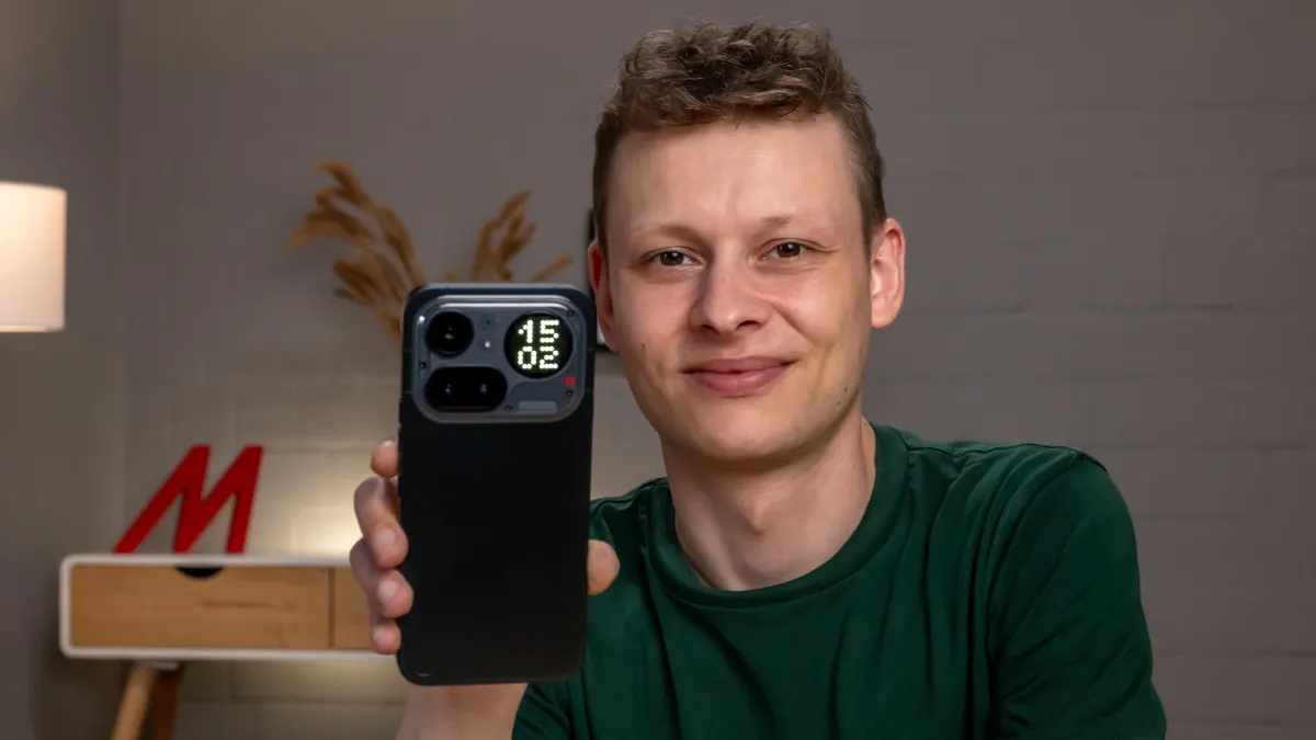 Alex hält das Nothing Phone (4a) Pro mit der Rückseite zur Kamera. Im rechten oberen Eck des Smartphones erkennst du die Uhrzeit auf der Glyph-Matrix.
