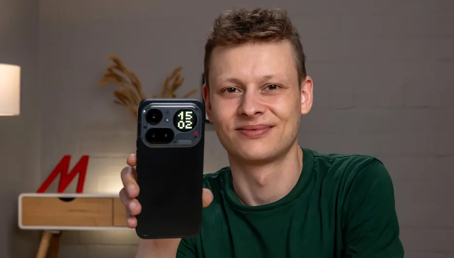 Alex hält das Nothing Phone (4a) Pro mit der Rückseite zur Kamera. Im rechten oberen Eck des Smartphones erkennst du die Uhrzeit auf der Glyph-Matrix.