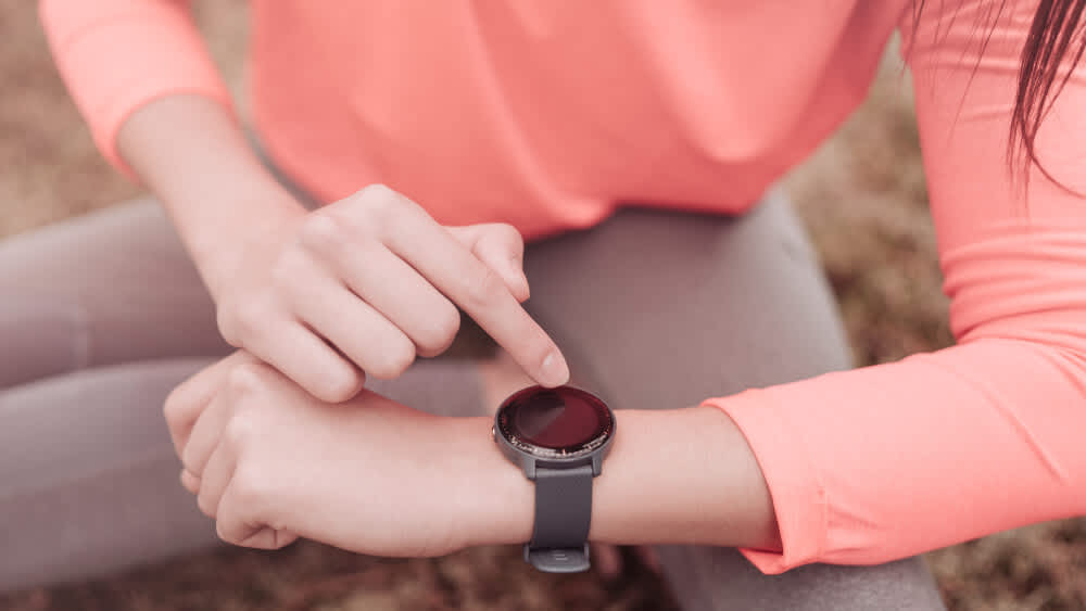 Frau in pinker Trainingsbekleidung zeigt auf ihre Smartwatch