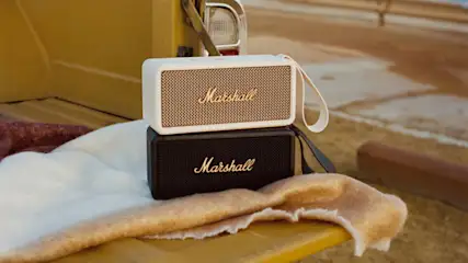 Zwei Marshall-Lautsprecher, ein weißer und ein schwarzer, liegen auf einer Decke auf einem gelben Untergrund.