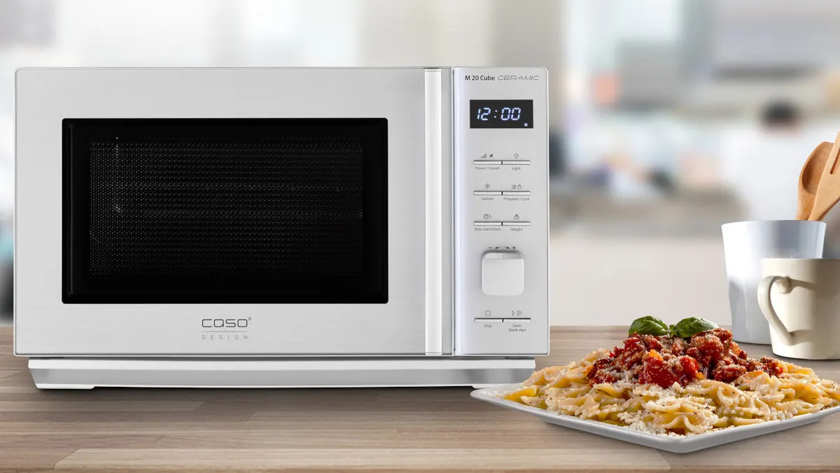 Die Mikrowelle Caso M 20 Cube Ceramic steht neben einem Teller mit Pasta auf einer Küchenarbeitsplatte.