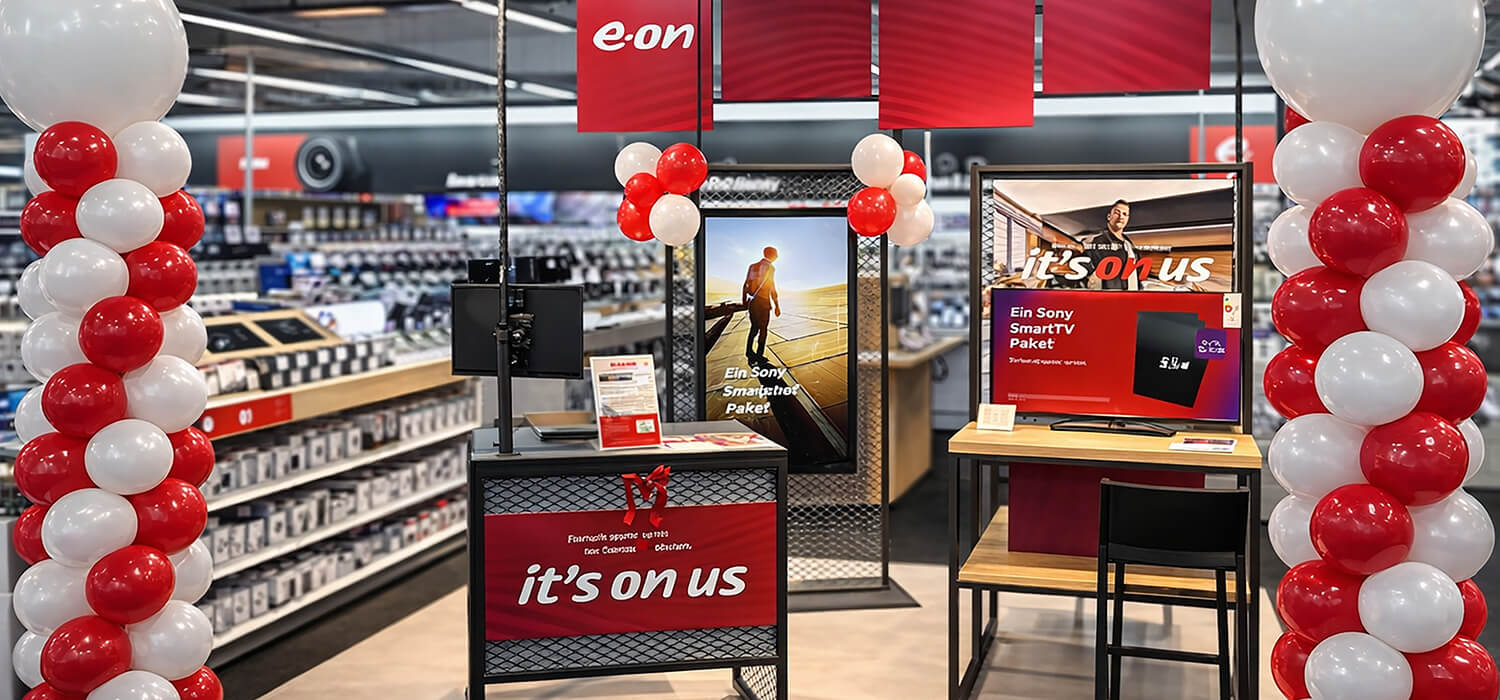 E.ON Aktionsstand im Elektronikmarkt mit rot-weißen Ballons, Monitoren und Infos zum Smart-Paket.