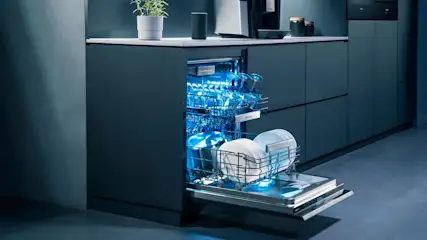 Offener Geschirrspüler mit blauem Licht, beladen mit Gläsern und Geschirr in einer modernen Küche.