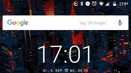 Ein Smartphone-Bildschirm zeigt die Uhrzeit 17:01, den 5. September und eine Google-Suchleiste vor einem Hintergrund aus Stadtgebäuden.