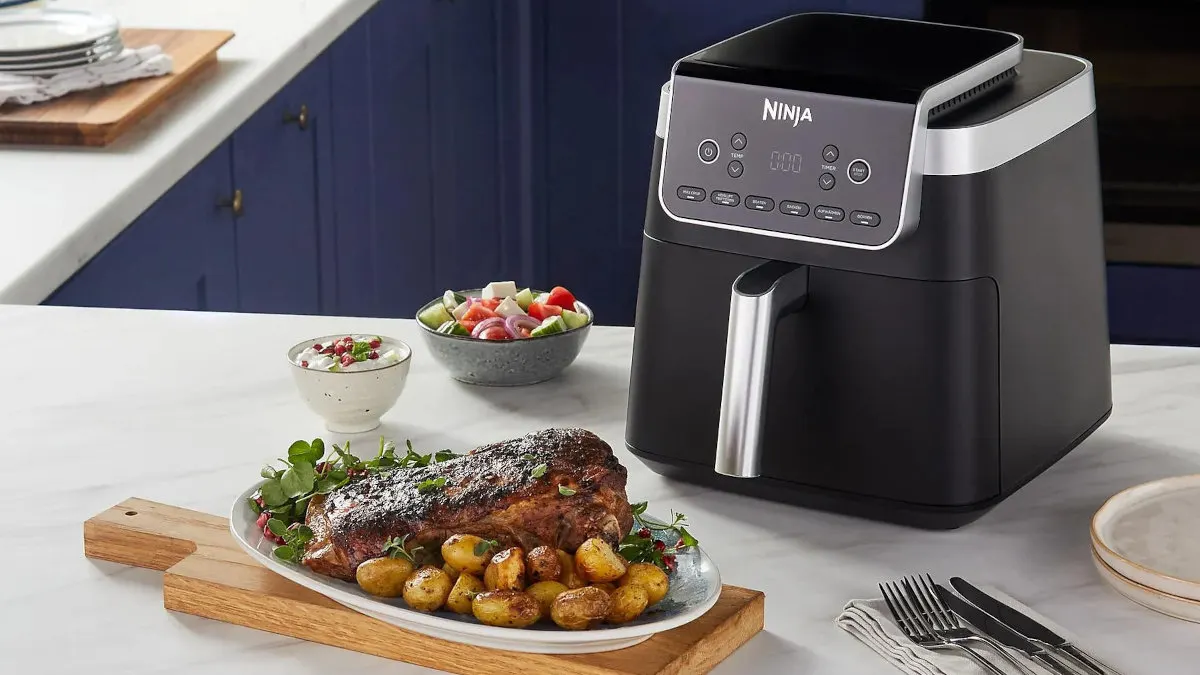 Die Heißluftfritteuse Ninja Max Pro AF180EU in einer Küche. Im Vordergrund ein Braten mit Kartoffeln und ein Salat mit Dip.