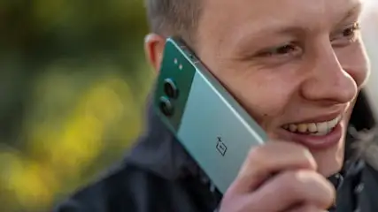 Ein Mann lächelt und telefoniert mit einem grünen Handy mit zwei Kameras vor einem verschwommenen, grünen Hintergrund.