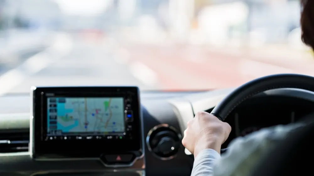 Innenraum eines Autos mit Navigationsgerät links und einer Person, die das Lenkrad hält, mit verschwommenem Blick auf die Straße.