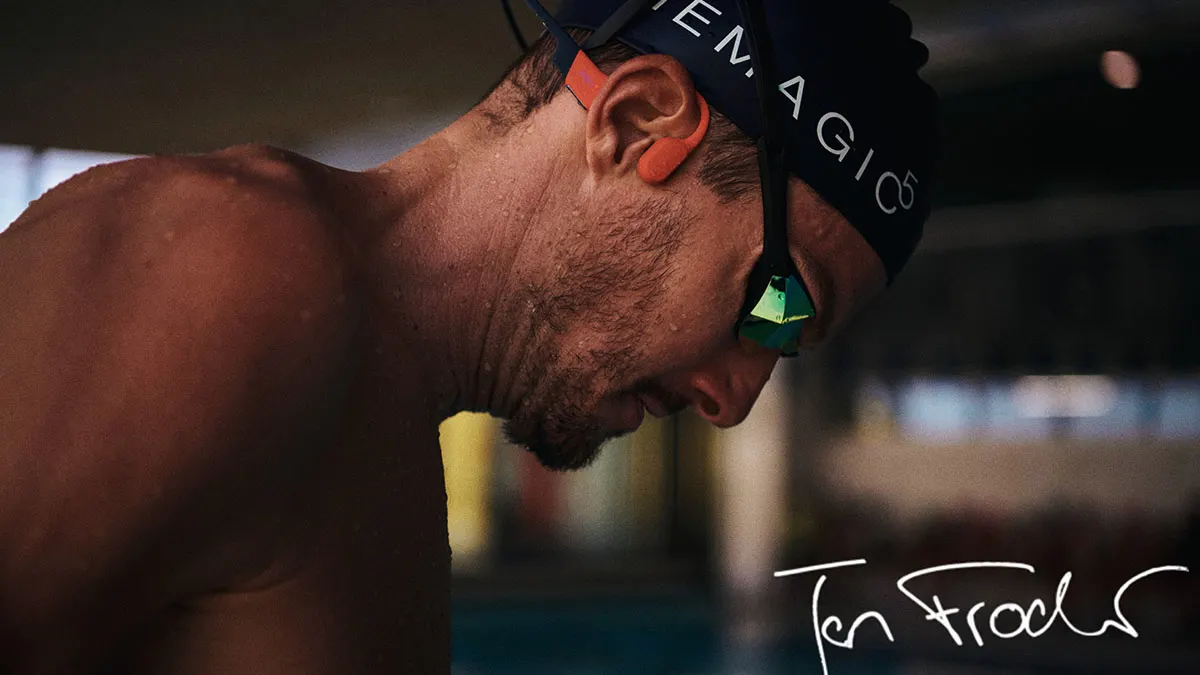 Ein Mann mit Badekappe und grüner Schwimmbrille blickt nach unten, mit Kopfhörern am Ohr und dem Wort "Ten Frode" im Vordergrund.