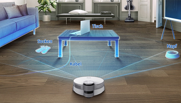 Ein Roboterstaubsauger steht auf einem Holzboden in einem Wohnzimmer mit Sofa, Tisch, Socken und einem Hundenapf.