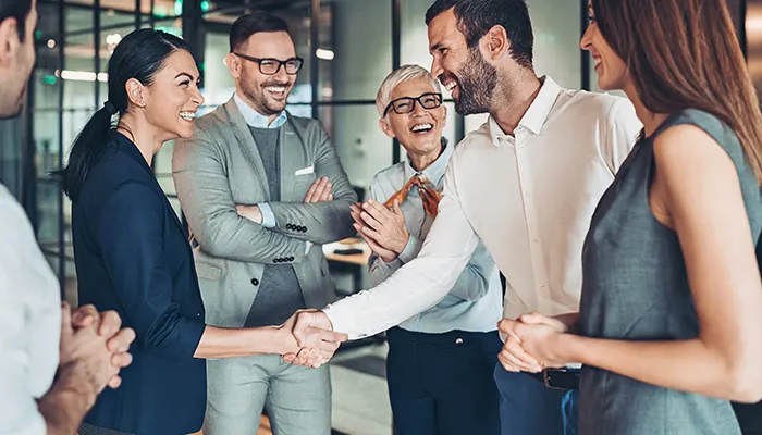 Eine Gruppe von sechs Personen in Businesskleidung lächelt und schüttelt sich die Hände in einem Büro.