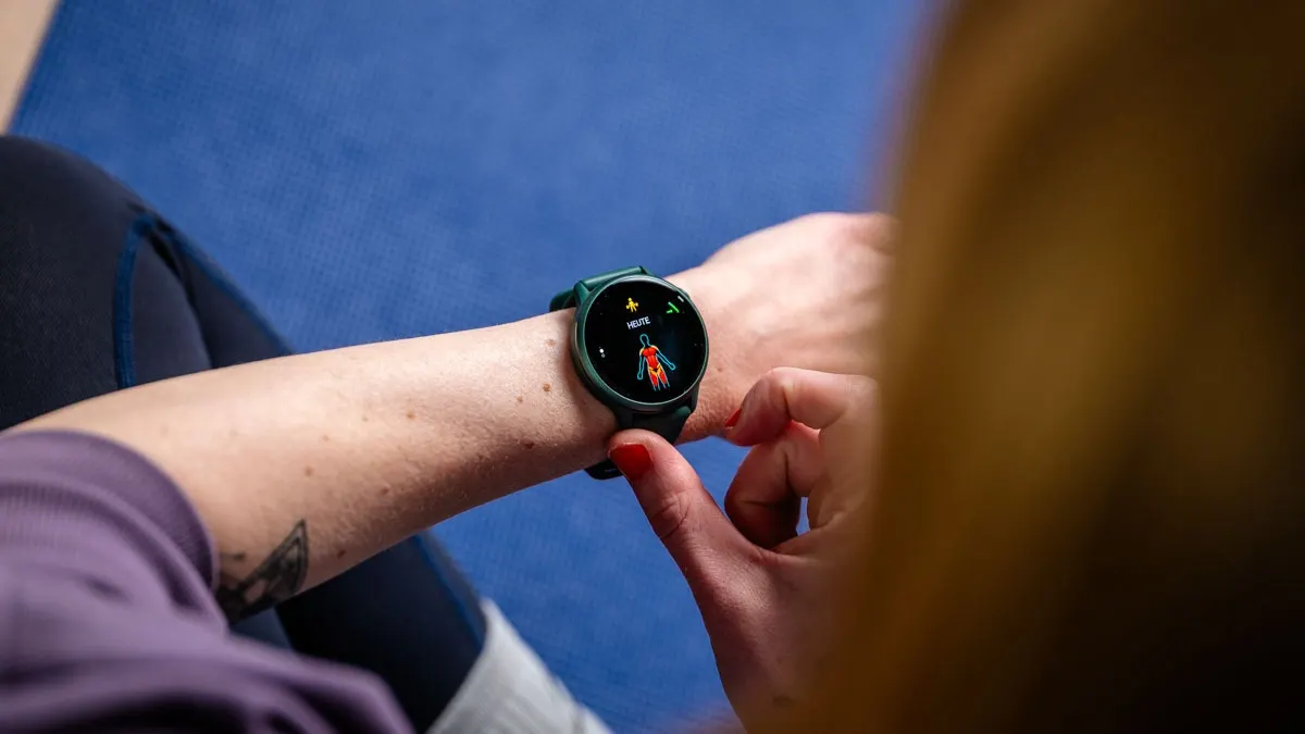 Eine Person tippt auf eine grüne Smartwatch mit einer roten menschlichen Figur auf dem Display. Blauer Hintergrund.