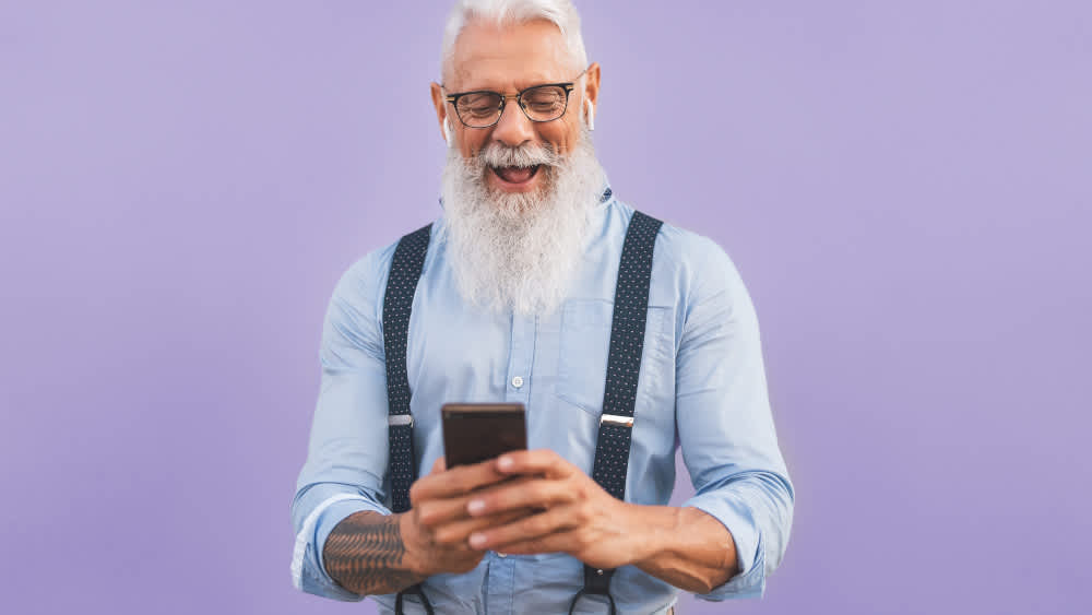 Ein alter Mann schaut begeistert auf ein Smartphone.