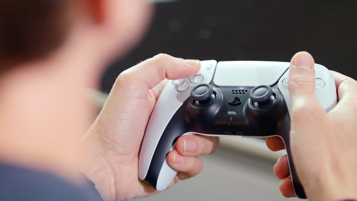 Ein PS5-Controller liegt in zwei Händen. Davor die verschwommenen Umrisse des Spielers.